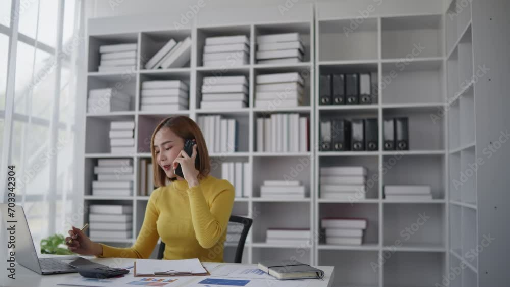 Businesswoman is talking to clients and colleague on the phone and working on laptop in office Businesswoman is talking to clients and colleague on the phone and working on laptop in office
