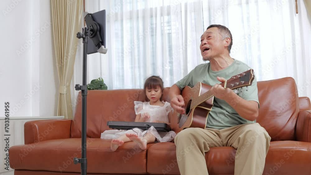 Grandpa and his little Asian granddaughter play a musical instrument Guitar and electronic piano together Show on social media online via tablet. Music band. Family concept. Grandpa and his little Asian granddaughter play a musical instrument Guitar and electronic piano together Show on social media online via tablet. Music band. Family concept.