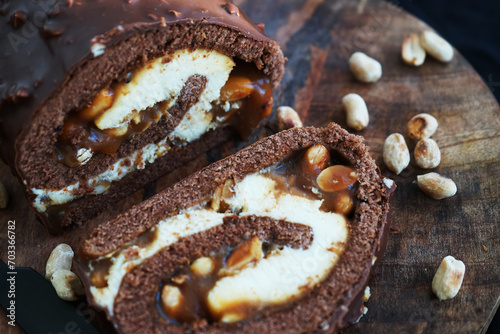 Chocolate roll with cream and caramel next to peanuts on a wooden tray on a dark background photo