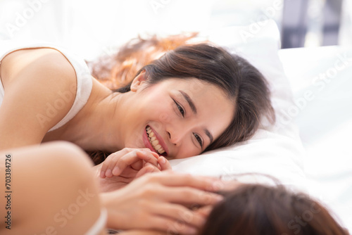 LGBTQ+ Asian couple laughing together at home. Affectionate young lesbian couple sharing a laugh while sitting on their bed at home. LGBTQ+ concept.