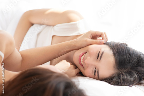 LGBTQ+ Asian couple laughing together at home. Affectionate young lesbian couple sharing a laugh while sitting on their bed at home. LGBTQ+ concept.