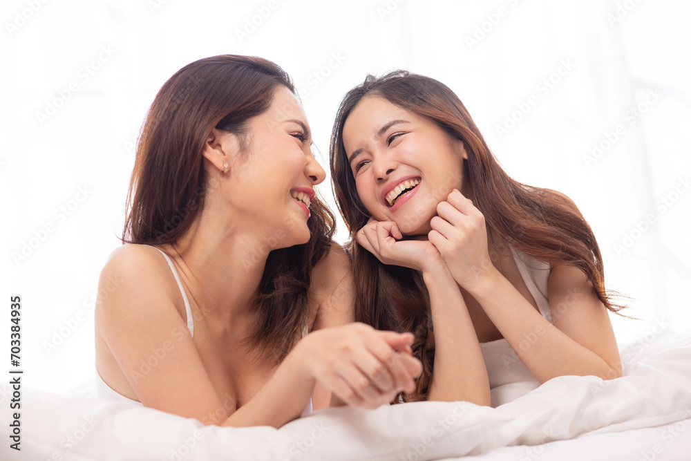 LGBTQ+ Asian couple laughing together at home. Affectionate young lesbian couple sharing a laugh while sitting on their bed at home. LGBTQ+ concept.
