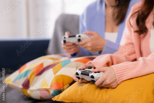 Two happy asian roommates sitting on couch in living room at home enjoy and excited holding console playing game together. photo