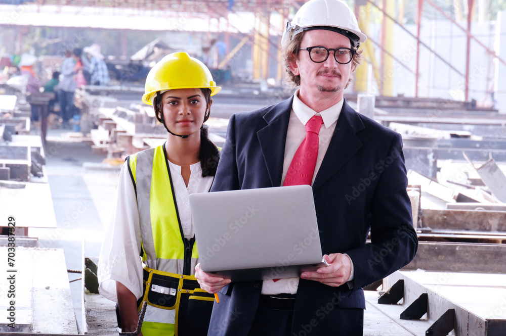 Engineer in safety helmet holding laptop working on job site.