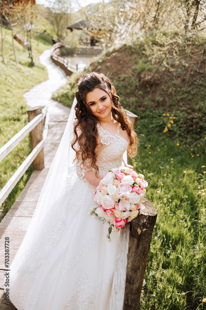 Curly brunette bride poses with a bouquet, near a wooden railing. Magnificent dress with long sleeves, open bust. Spring wedding