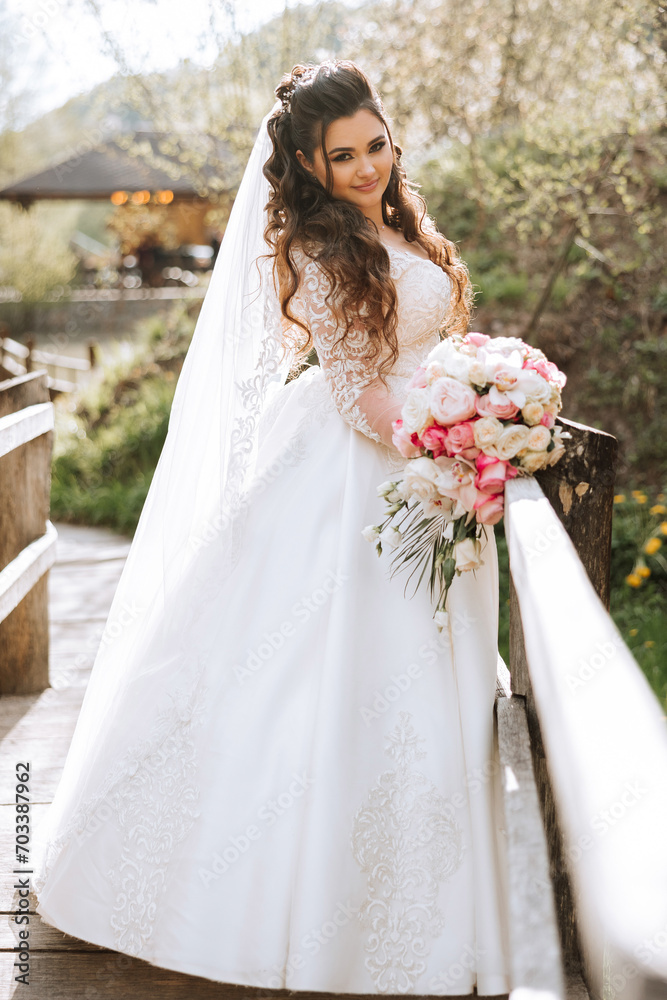 Curly brunette bride poses with a bouquet, near a wooden railing. Magnificent dress with long sleeves, open bust. Spring wedding Curly brunette bride poses with a bouquet, near a wooden railing. Magnificent dress with long sleeves, open bust. Spring wedding