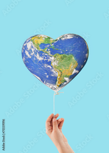 Planet Earth in heart-shaped balloon held by child\'s hand on isolated pastel blue background. Minimal creative concept of travel, sustainablity, love, ecology. Earth Day card. World provided by NASA.