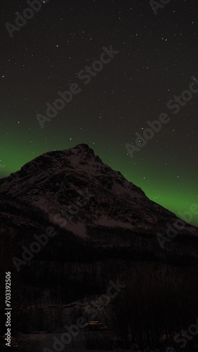 Aurora borealis in the dark night sky over snowy mountains near Tromso, Norway