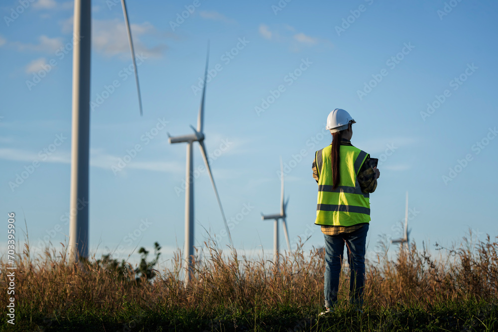 worker with turbine. Back view of female engineers standing against turbines on wind turbine farm. worker with turbine. Back view of female engineers standing against turbines on wind turbine farm.