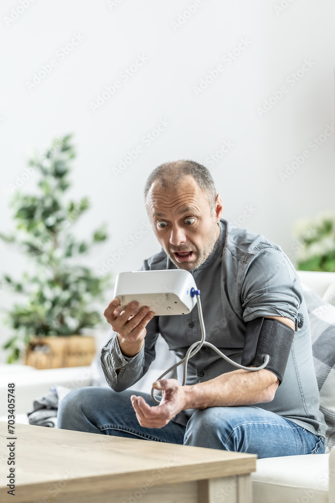 Shocked mature man after measuring blood pressure with a measuring device because of a bad result