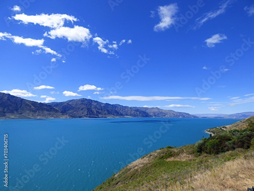 Lake Wanaka, New Zealand on a beautiful sunny day. Calm blue water with mountains in the background and clear skies © Anna