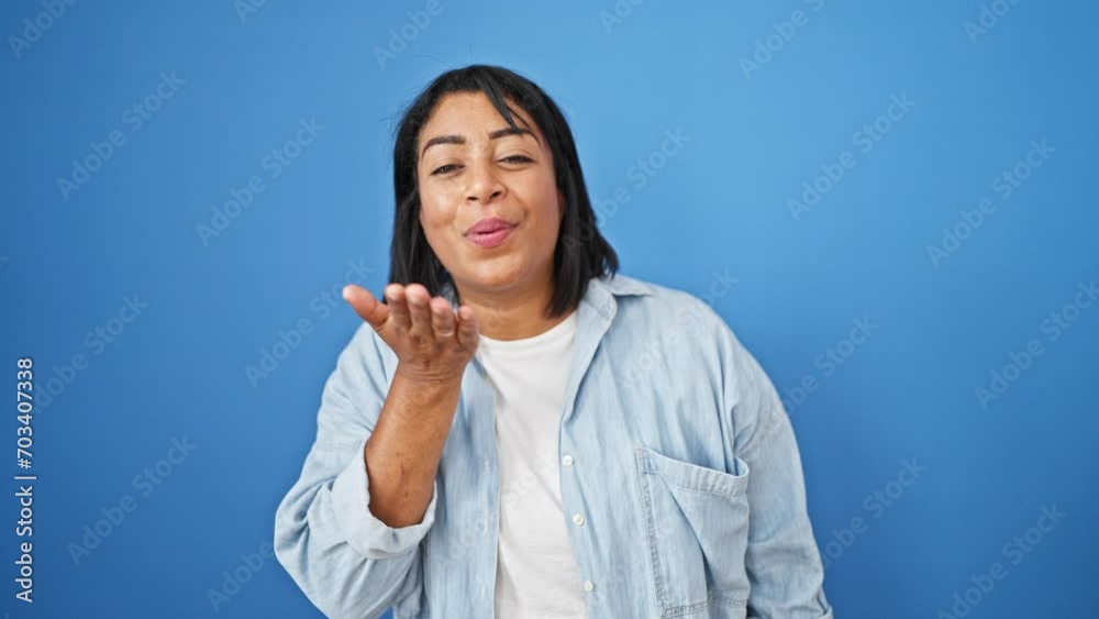 Hispanic middle-aged woman blows a kiss against a blue isolated background, expressing joy and friendliness. Hispanic middle-aged woman blows a kiss against a blue isolated background, expressing joy and friendliness.