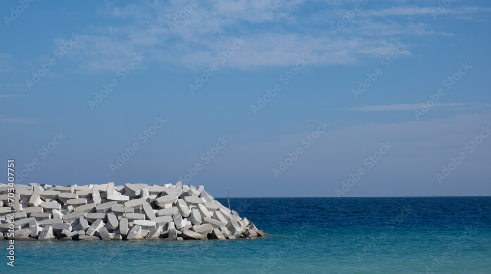 Sea breakwater with cement blocks. Marine infrastructure. Blue calm sea and sky