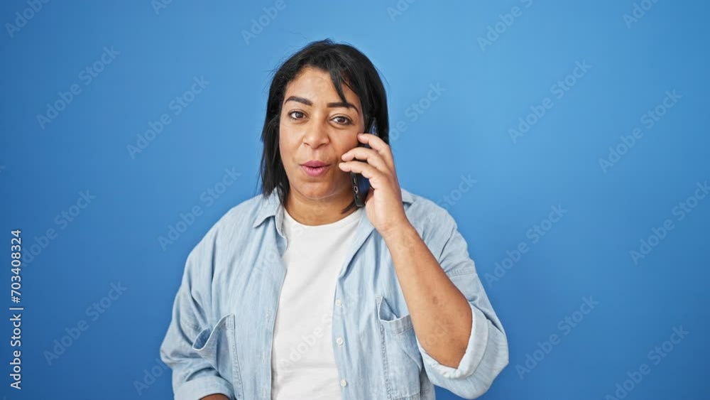 Smiling middle-aged hispanic woman talking on a smartphone with a blue background Smiling middle-aged hispanic woman talking on a smartphone with a blue background
