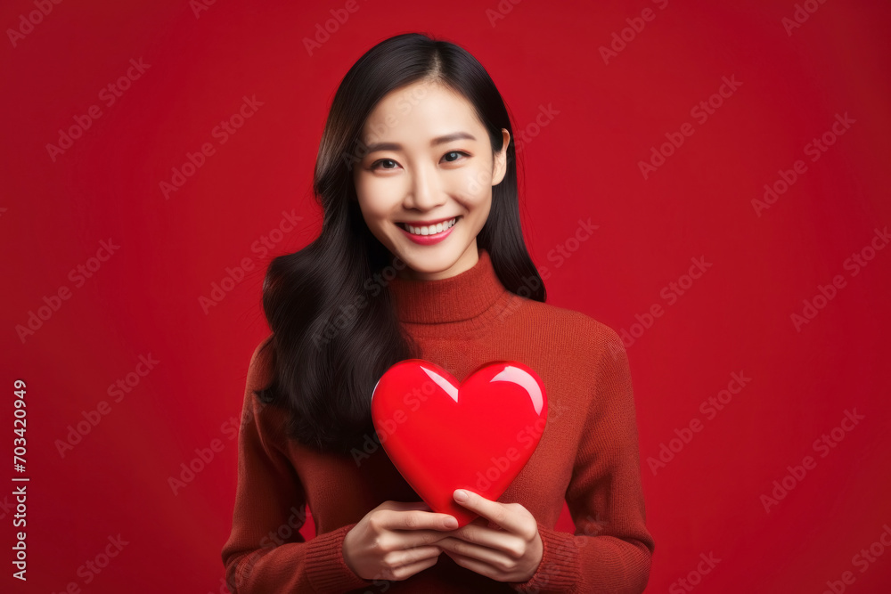 A beautiful woman with a heart-shaped red toy against a red backdrop A beautiful woman with a heart-shaped red toy against a red backdrop