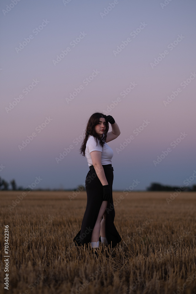Chica atractiva posa parada en el campo durante un colorido atardecer Chica atractiva posa parada en el campo durante un colorido atardecer