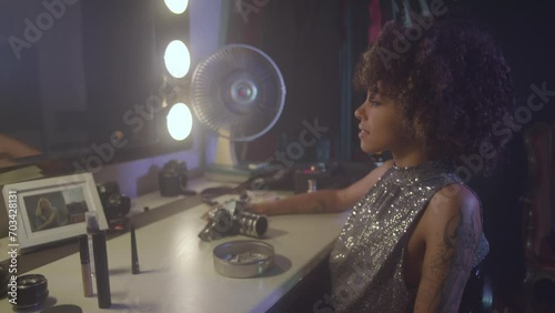 Afroamerican young woman tasting a cigarette in front of an old fashioned mirror, wearing a glitter dress. photo