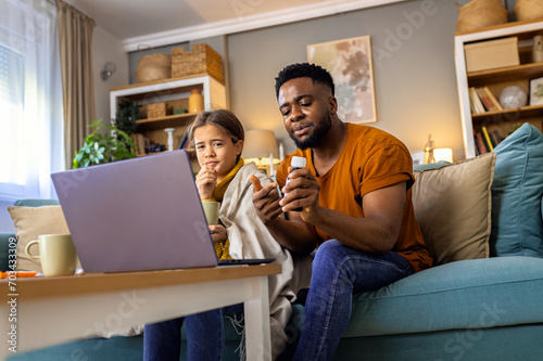 African American father and daughter with fever sitting at home and have online consultations with the doctor via laptop.