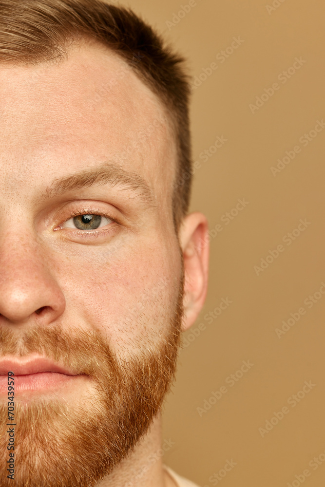 Obraz premium Half portrait of beautiful calm young man looking at camera. Male model serene and composed. Against beige background. Concept of beauty treatment, selfcare and hygiene, cosmetic, spa.