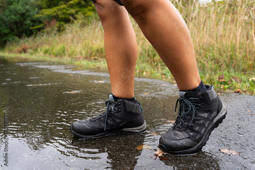 Close up of legs of hiker woman in boots trying to pass a small puddle in the middle of the trail on his hiking route in Ireland