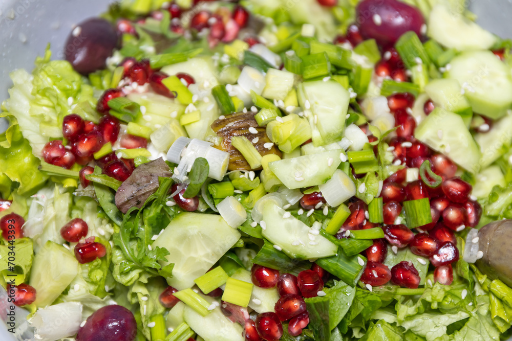 Fresh salad with a mix of fruits and vegetables. Lettuce, arugula, baby spinach, cucumber, pomegranate, olives and fresh onion mixed and poured with olive oil