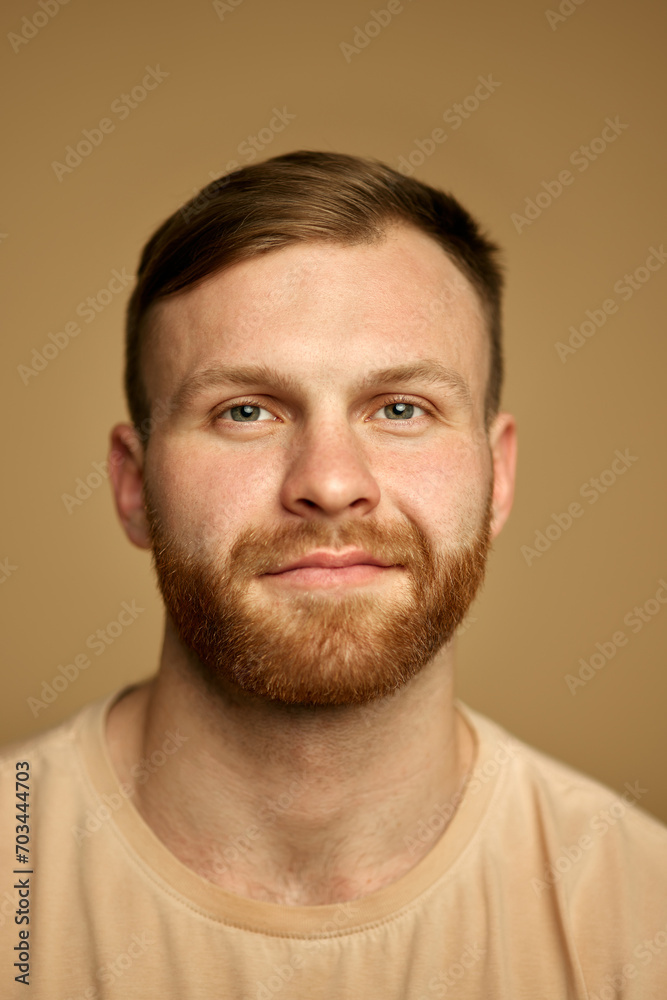 Vertical portrait of young handsome redhead man with beard smiling looking at camera against sandy color studio background. Concept of beauty treatment, selfcare and hygiene, cosmetic, spa. Vertical portrait of young handsome redhead man with beard smiling looking at camera against sandy color studio background. Concept of beauty treatment, selfcare and hygiene, cosmetic, spa.