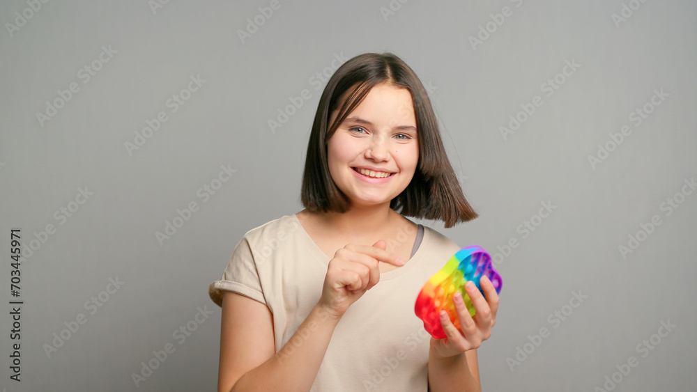 Young latin teenager female girl playing with pop-It kids toy, smiling isolated on gray background. Copy space Young latin teenager female girl playing with pop-It kids toy, smiling isolated on gray background. Copy space