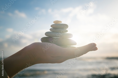 Concept of harmony, positive mind, mental health. Balance of stones on a human hand, close-up against the sea and sun. Enjoying life, balancing body, mind, soul and spirit.