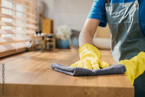 Maid in protective glove wipes wood table in cozy kitchen. Using professional cleaning products for perfect home tidiness. Cleaner working safety glove hygiene routine. Maid housekeeping concept.
