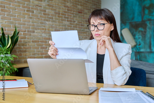 Φωτογραφία Serious mature businesswoman reading official letter, sitting in office