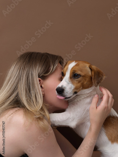 Cute woman kisses and hugs her Jack Russell terrier dog on a brown background. Sweet love between owner and pet