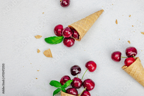 Ripe sweet cherries in waffle cones on light stone concrete background. Flat lay, vintage napkin