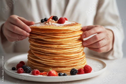 Woman hands making stack of blini or crepes with berries on top on white plate on white surface photo