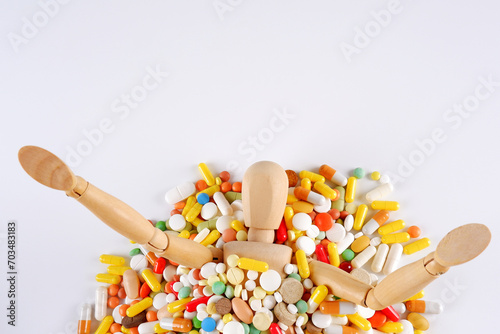 A wooden mannequin, strewn with colorful pills, is drowning in a pile of medicines on a white background.The unhealthy concept of drug addiction, articles about the dangers of drugs.Copyspace