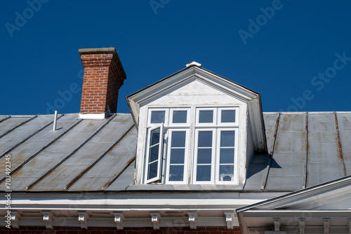 A red brick chimney and a dormer window in an old metal roof photo