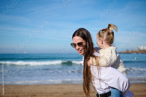 Mom and child girl kid enjoy and fun outdoor lifestyle on the beach. Mother giving piggyback to her lovely daughter