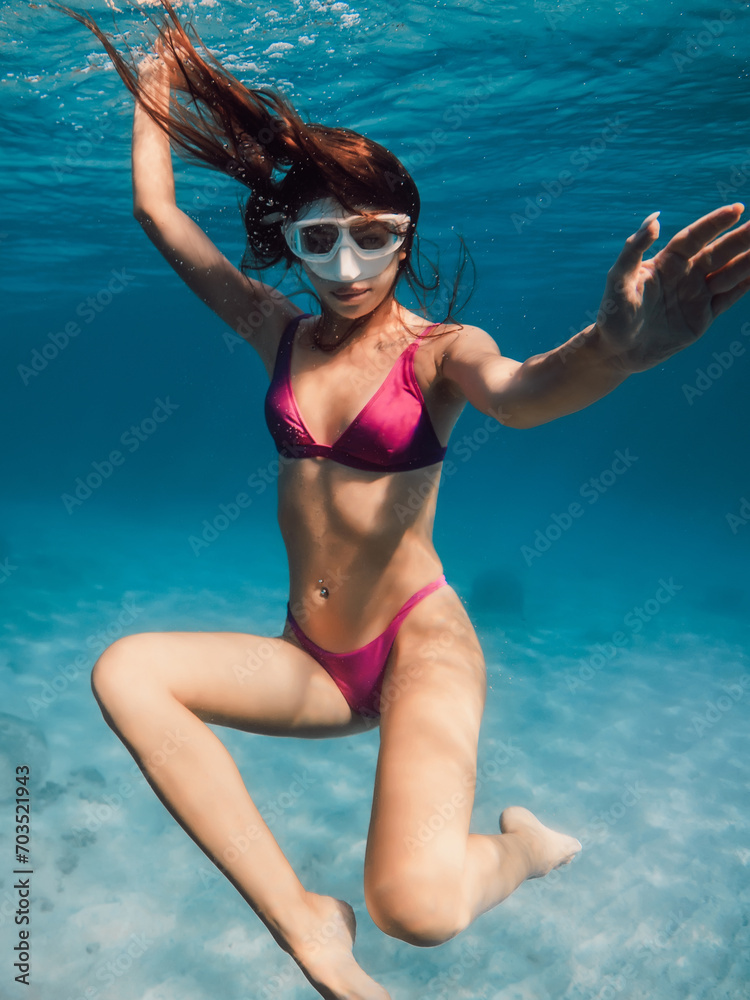 Fototapeta premium Young woman in bikini swimming underwater in blue ocean.