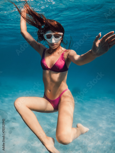 Young woman in bikini swimming underwater in blue ocean.