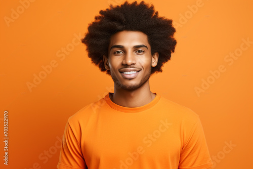 Young man with afro hair wearing orange t-shirt smiling on orange background. Generative AI. photo
