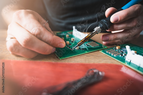 An engineer is repairing a broken electronics board. Analyzing what is broken. Soldering a resistor. Close up.