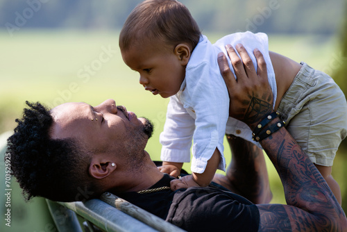 Close up portrait of afro american father kissing multiracial baby. Father hug Biracial child. Father with Biracial baby outdoor. Tender fathers hand carrying multiracial baby. © Volodymyr
