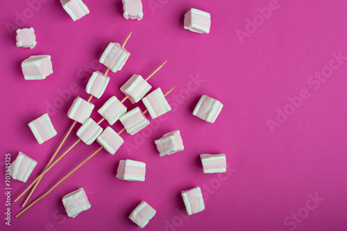 White and pink marshmallows on skewers on a bright pink background. Horizontal, copy space.