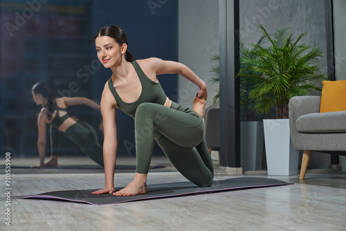 Happy caucasian woman having yoga practice at home after hard working day. Flexible pretty woman making stretching on rug in twisting position, meditating alone in evening. Concept of yoga practice.