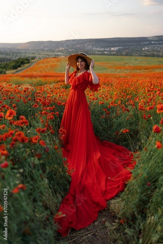 Woman poppy field red dress hat. Happy woman in a long red dress in a beautiful large poppy field. Blond stands with her back posing on a large field of red poppies. © svetograph