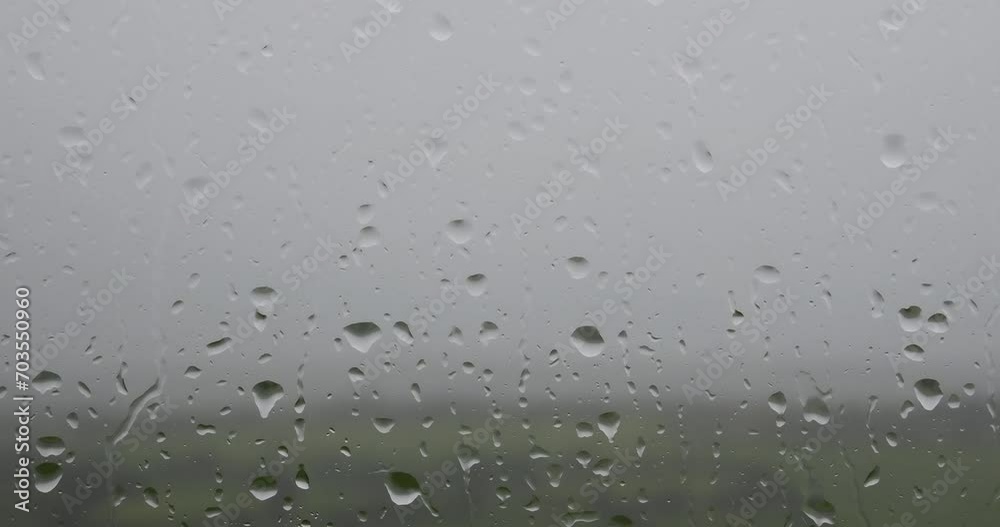 A video of raindrops on a window, with a green field and trees in the background. A video of raindrops on a window, with a green field and trees in the background.