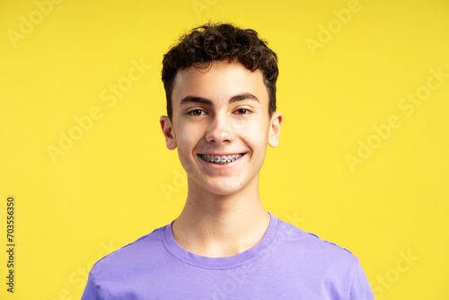 Closeup portrait of smiling confident  boy with dental braces on teeth looking at camera isolated on yellow background. Health care, orthodontic concept photo