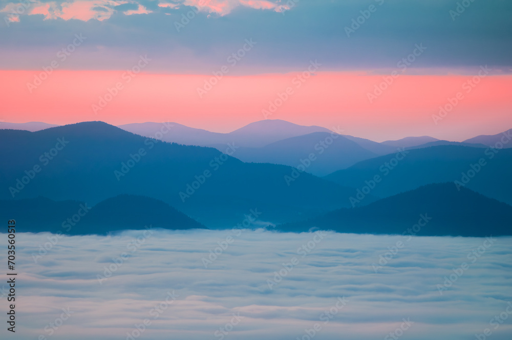 A sea of fog and silhouettes of mountains on the background of the sky in the colors of the sunrise