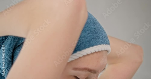 Young caucasian female wrapping hair in blue cotton towel after morning shower. Close up view of smiling pretty lady putting towel on head in bathroom, slow motion. Concept of body care routine.