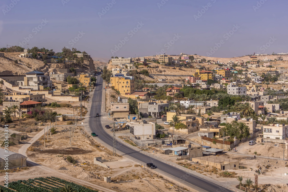 The aerial view on the road, palm tree plantation, and residential houses at Palestinian town of Jericho, West Bank, Palestine, during the hot summer day.