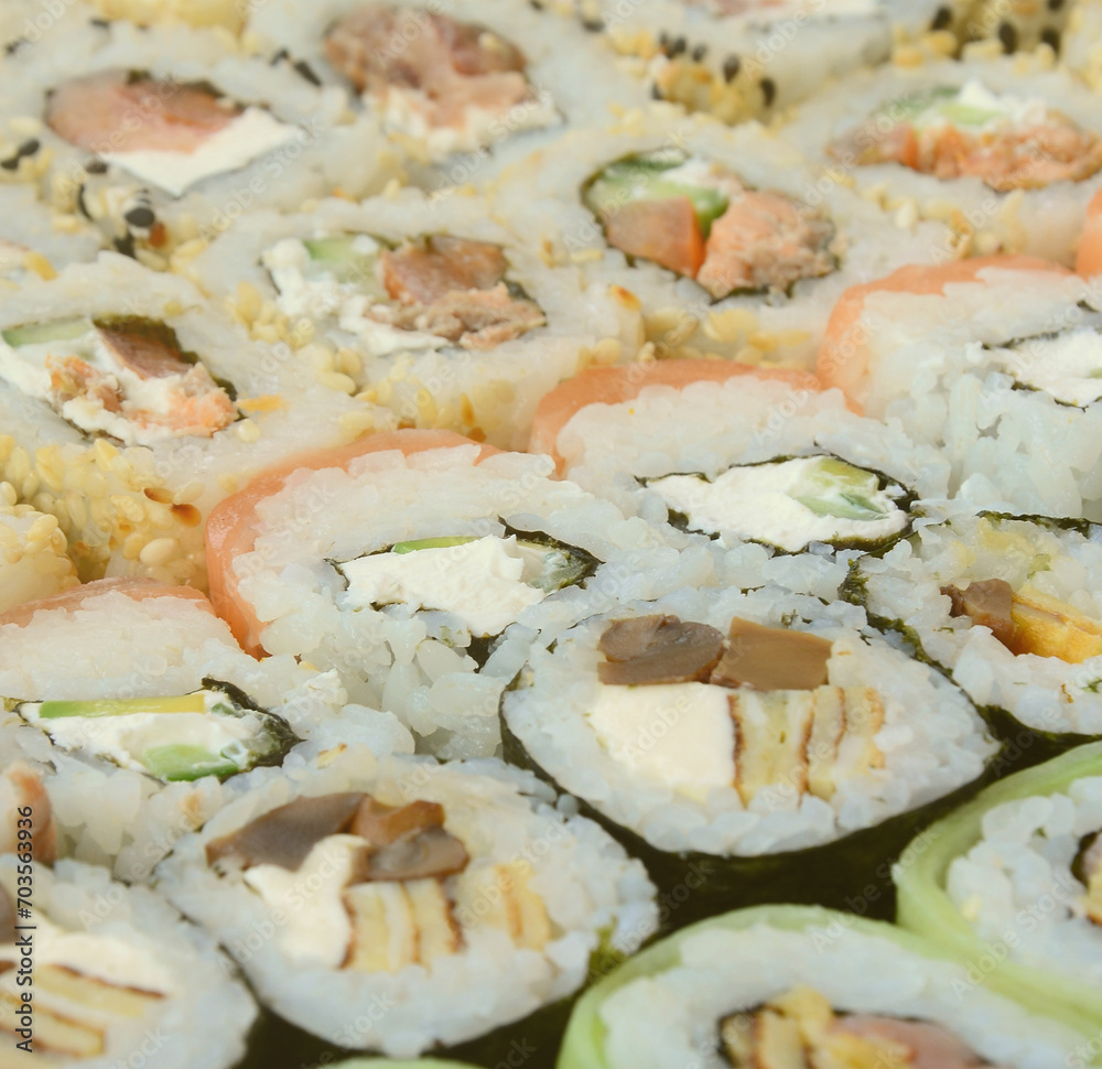 Close-up of a lot of sushi rolls with different fillings lie on a wooden surface. Macro shot of cooked classic Japanese food with a copy space. Close-up of a lot of sushi rolls with different fillings lie on a wooden surface. Macro shot of cooked classic Japanese food with a copy space.